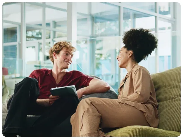 Two people having a thoughtful conversation while seated in a bright workplace lounge.