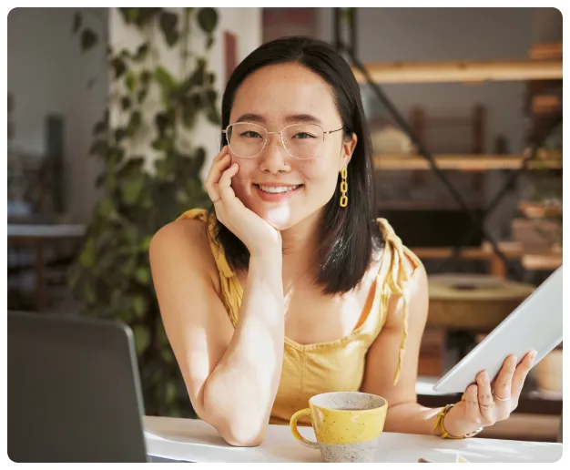 A person smiling while seated at a table with a laptop and a drink.